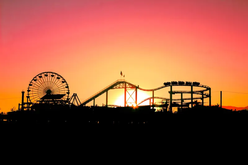The Ferris wheel and roller coaster on Santa Monica Pier silhouetted against an orange sunset