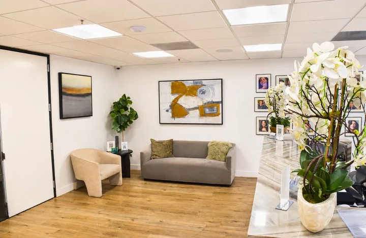 Waiting lounge with a grey sofa, a cream armchair and gold framed art